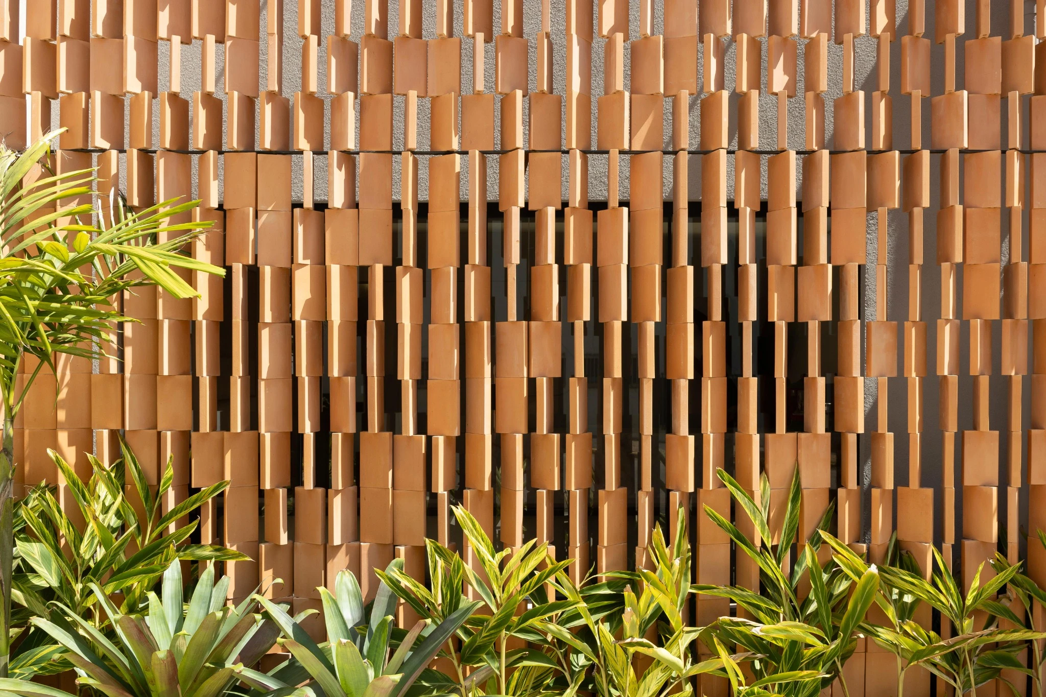 Detalhe de fachada de cerâmica com vegetação e luz natural