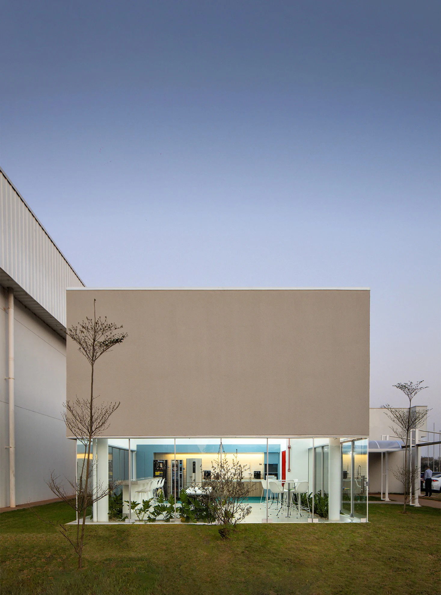 Denso Casual Food ao entardecer, com volume branco e térreo iluminado aberto ao jardim