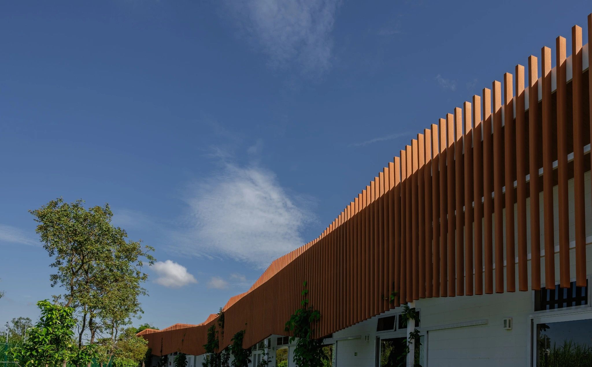Eco Escola Jardim: fachada com brises cerâmicos e jardim sob céu azul