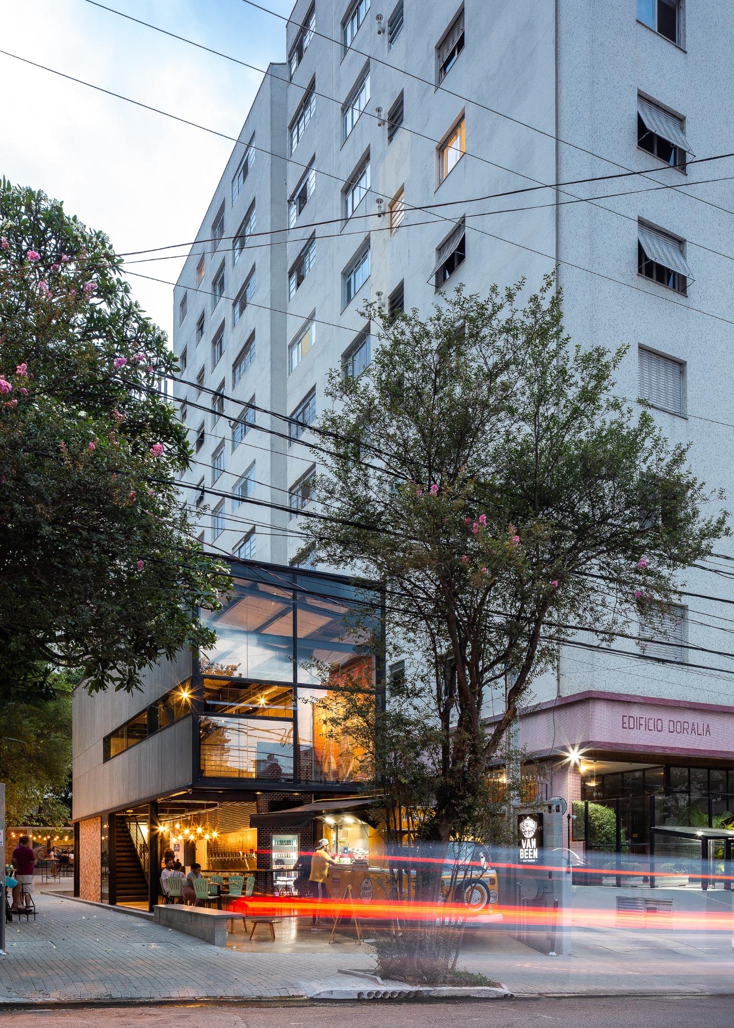 Cervejaria Van Been iluminada ao entardecer, com estrutura metálica e movimento da rua